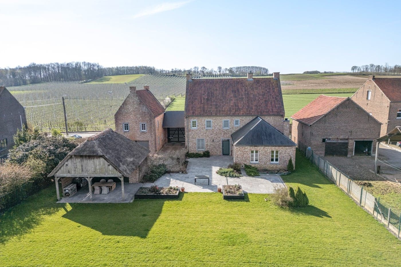 Een luchtfoto van een verzorgde hoeve met gazon, terras en tuinpaviljoen
