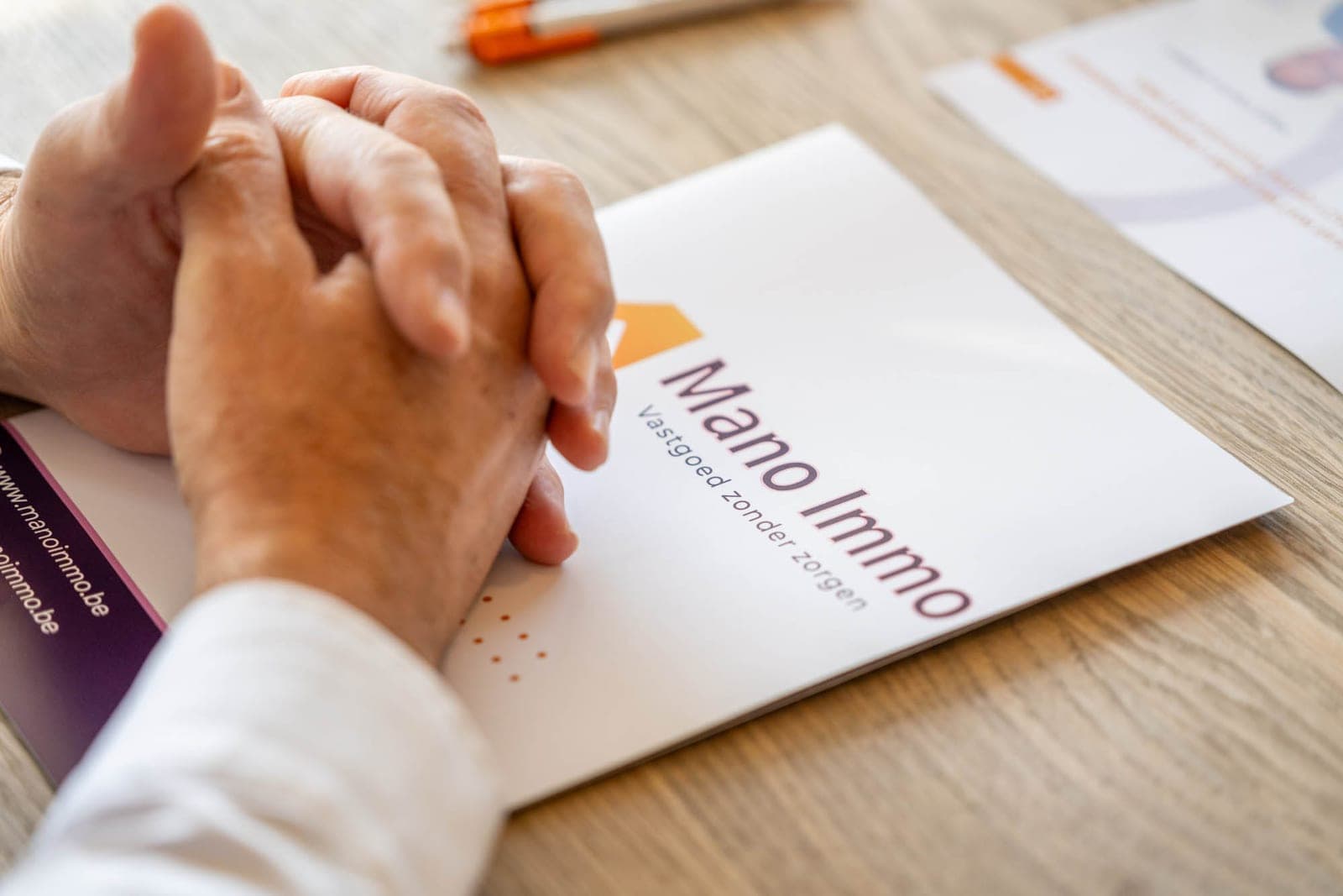 Handen op een document van Mano Immo aan tafel