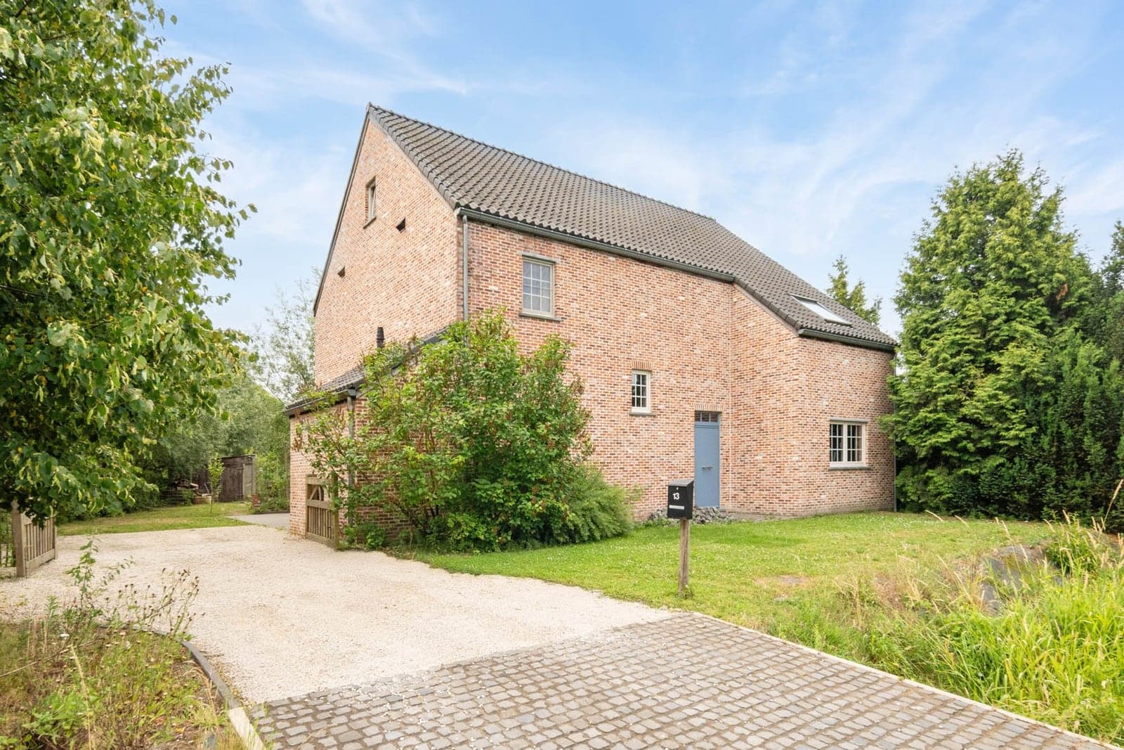 Een bakstenen woning met blauwe voordeur tussen het groen in Limburg