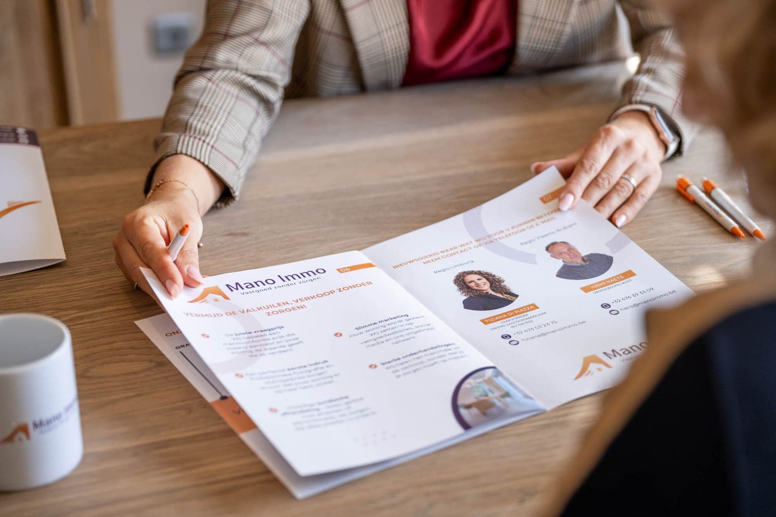 Tiziana overloopt de brochure van Mano Immo met een klant, met pen in de hand